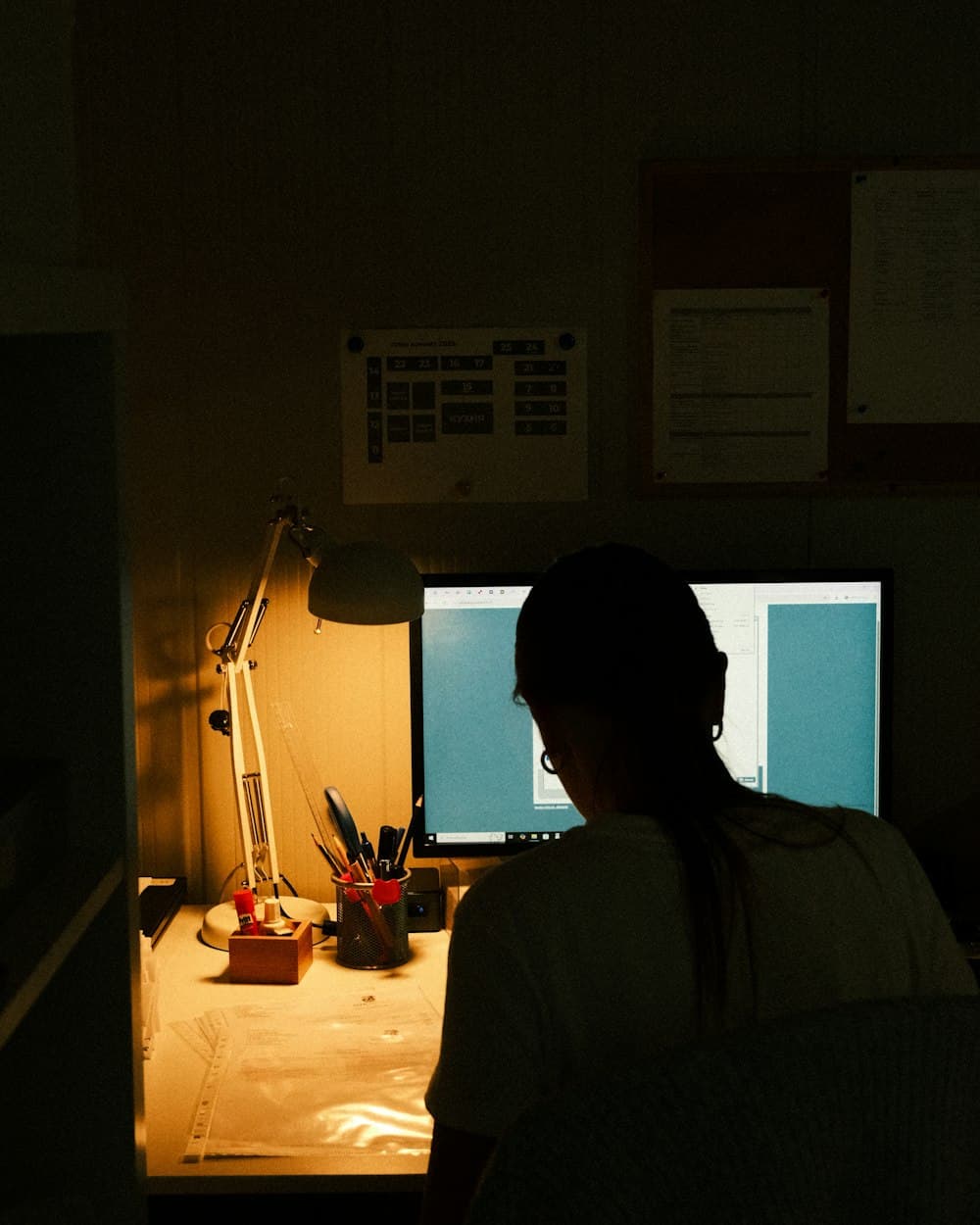 A designer at a desk at night, lit by a lamp and a monitor