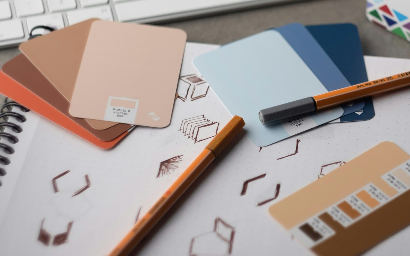 Colour swatch cards and orange pens on a sketchbook of geometric logo studies