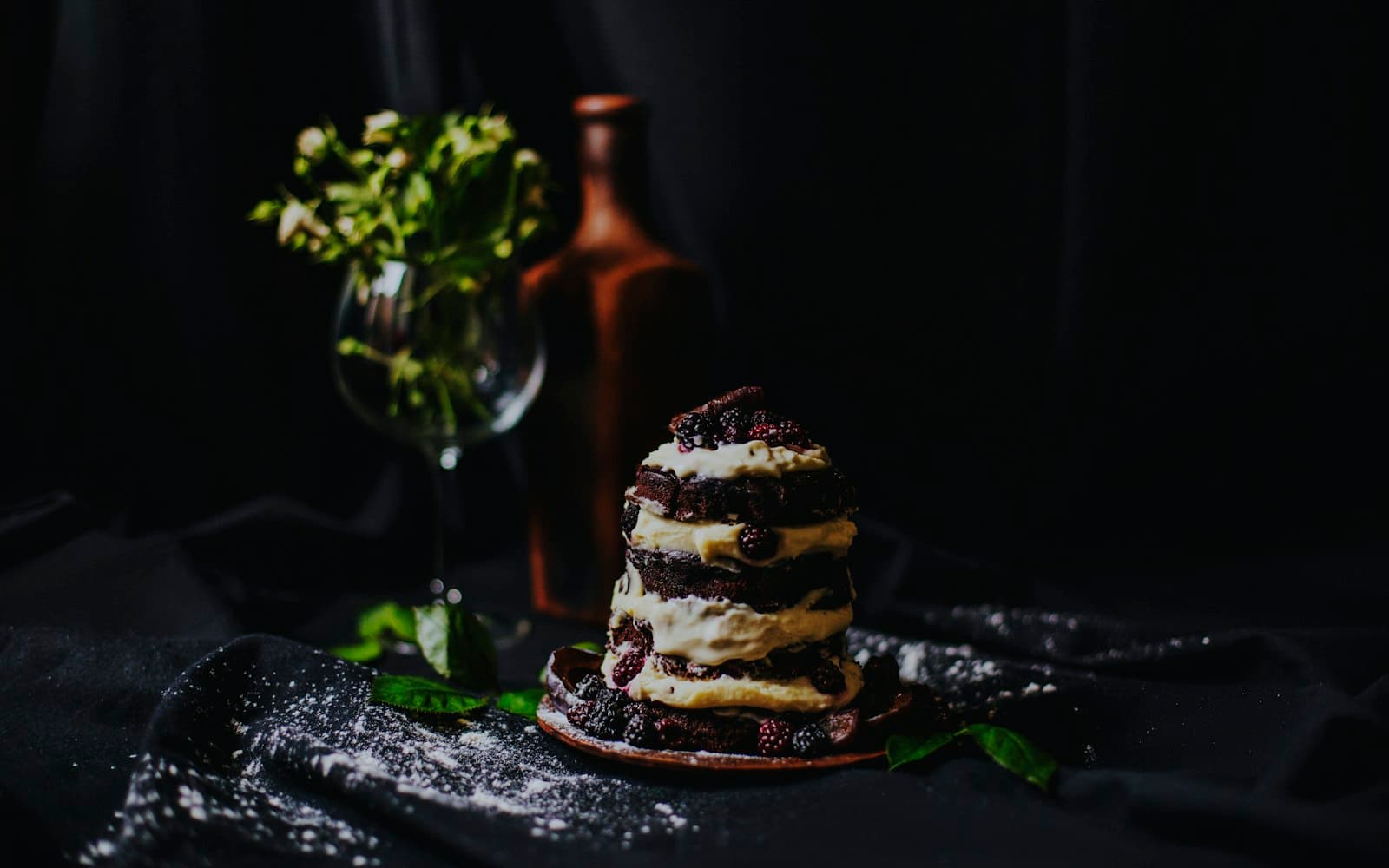 A moody product shot of a blackberry chocolate cake on dark cloth