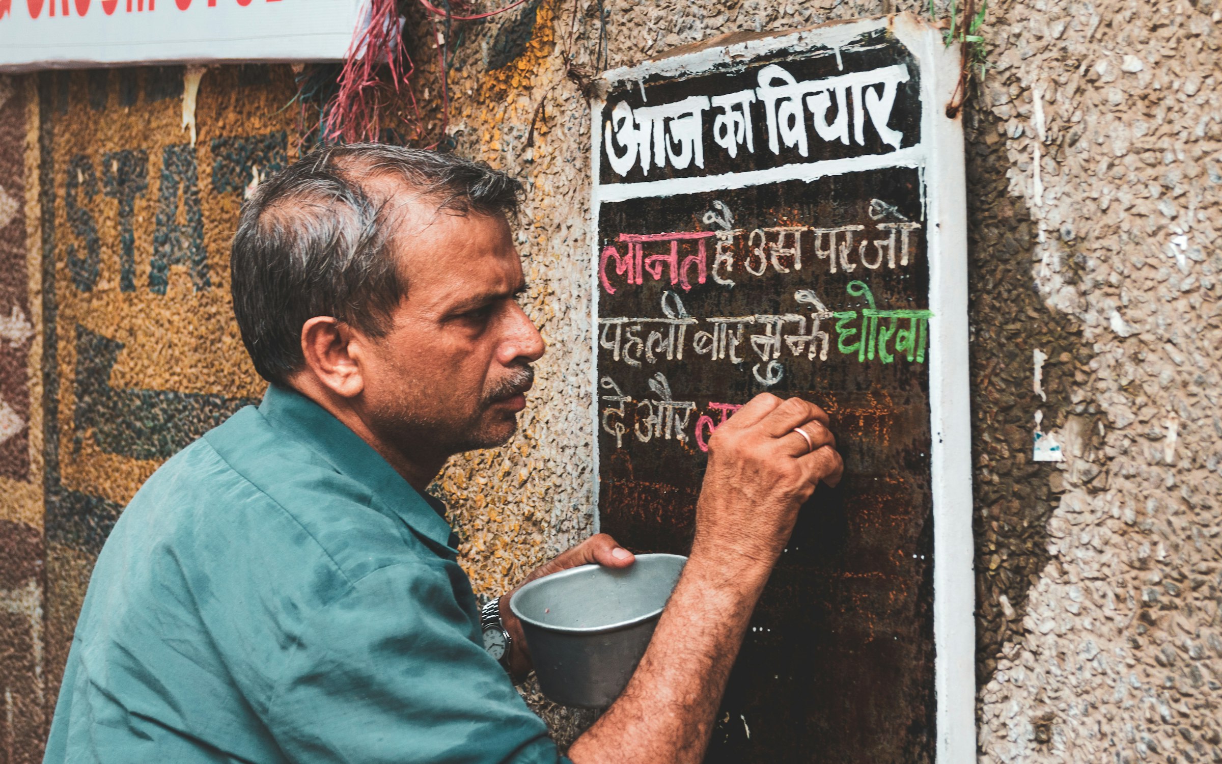 A sign painter hand-lettering a Hindi board on a wall in Old Delhi