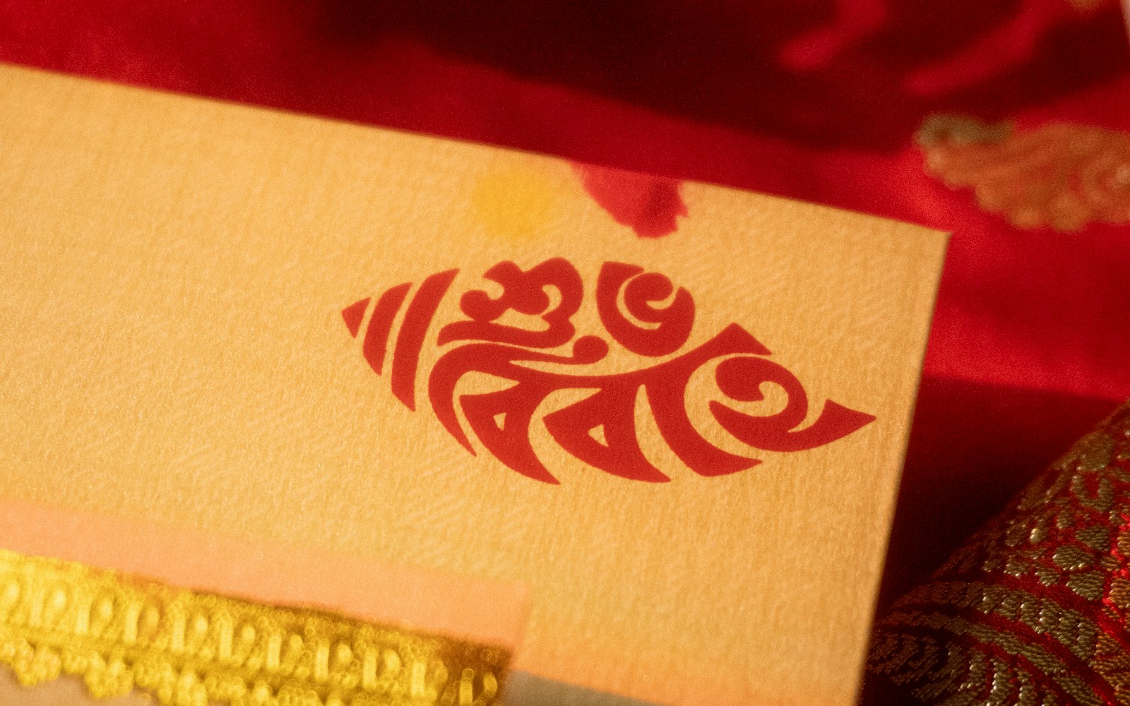 A Bengali wedding card with red calligraphy and gold lace on red silk