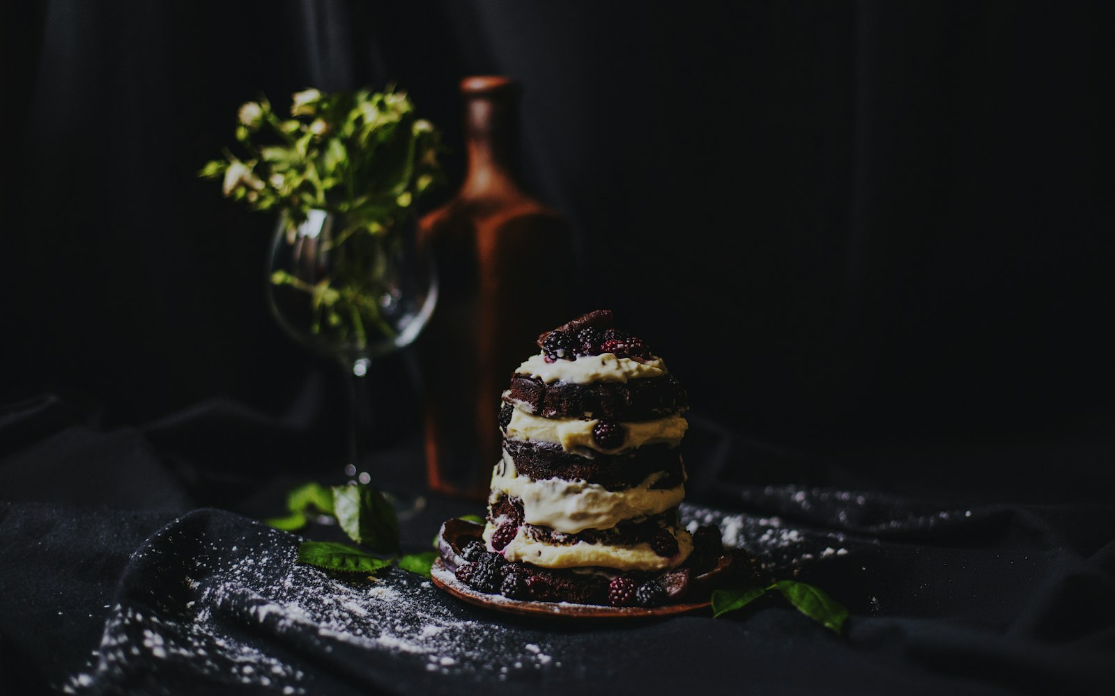 A moody product shot of a blackberry chocolate cake on dark cloth
