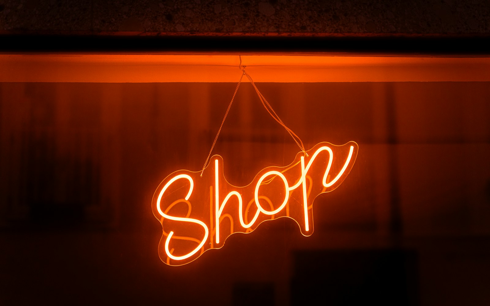 An orange neon "Shop" sign glowing in a dark window